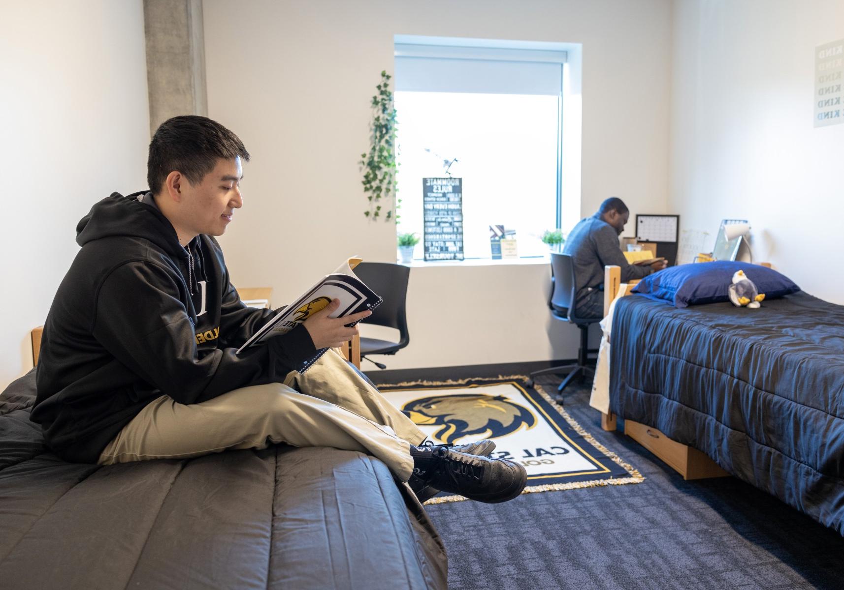 Student sitting on their bed reading, their roommate sits at a desk.