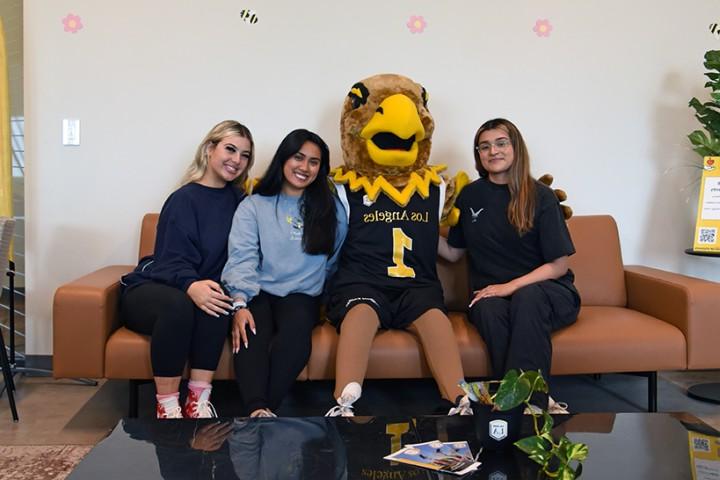 Eddie the Golden Eagle sitting on a couch with three student assistants.