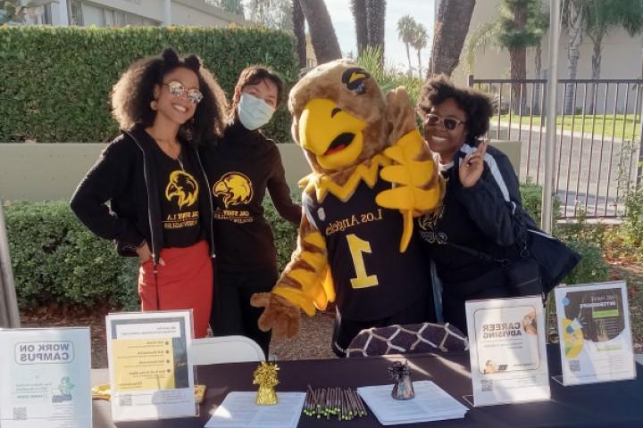 Career advisors, students and campus mascot Eddie smile while at a booth outside the 职业中心