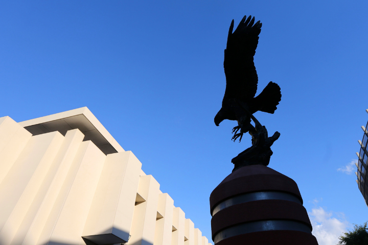 Eagle statue and white building behind. Backdrop is a blue sky 
