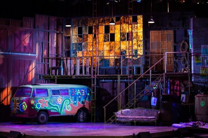 A wide shot of a past production of Hair, complete with Volkswagen bus onstage.