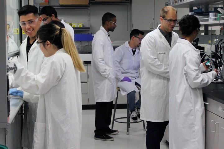 faculty, students in lab coats and safety glasses work in lab