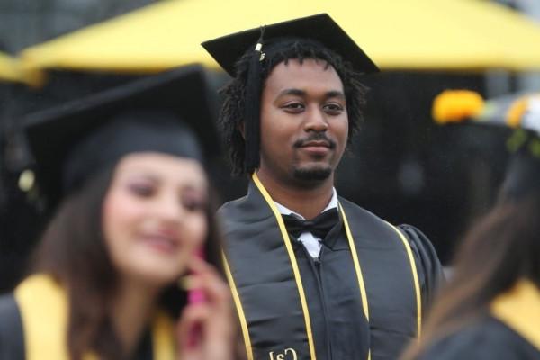 Image of a Black male student in Commencement regalia with a stoic expression on his face. 