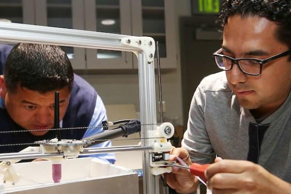 Image of two engineering students looking at a metal frame device intently. 